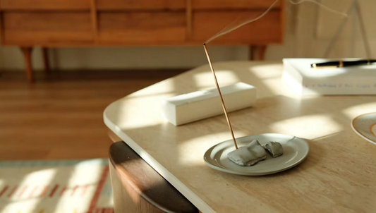 Handmade ceramic incense holder with burning stick on marble table in sunlit home office, with warm sunlight filtering through the window for a calm workspace vibe.