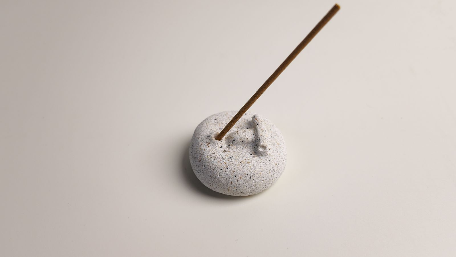A minimalist stone incense holder shaped like a human face, holding a burning incense stick.